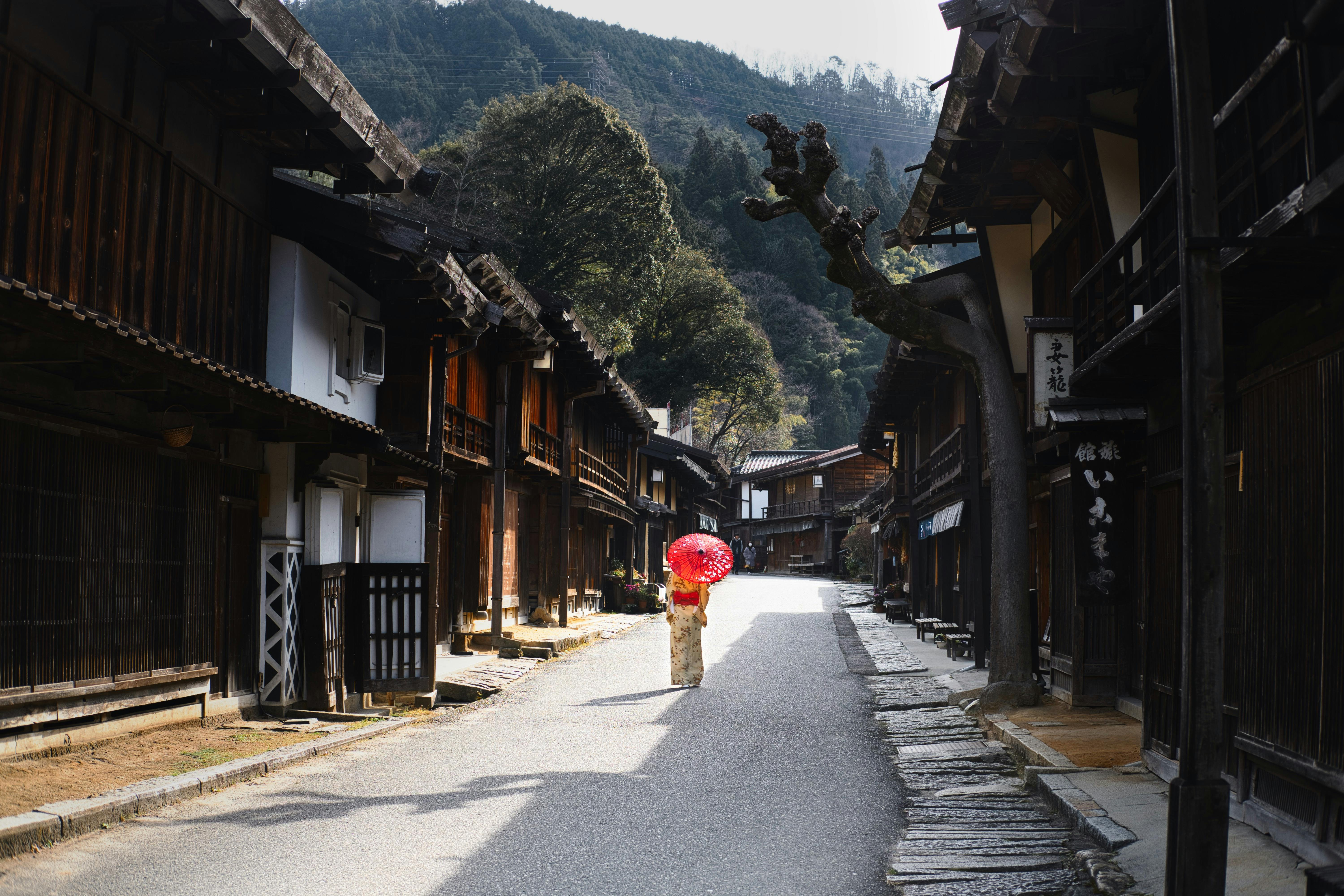 Person with red umbrella walking through traditional Japanese post town